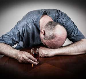 Alcoholic man face down on table with a shot of whiskey in his hand.