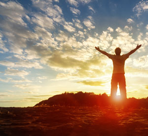 Man with arms held high looking out at the sunrise.