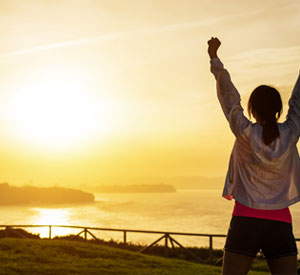 Victorious woman, arms raised high, looking toward the sunset.