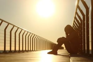 Drug Rehab Oxnard CA - Sad teenager girl depressed sitting in the floor of a bridge on the beach at sunset.